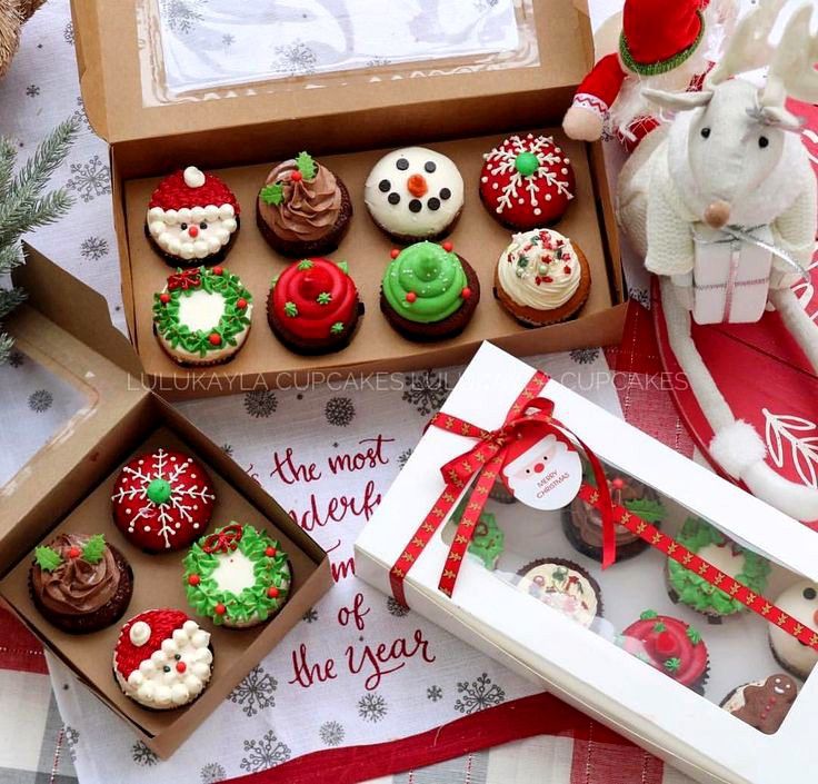 several decorated cupcakes in boxes on a table next to a stuffed animal and christmas decorations