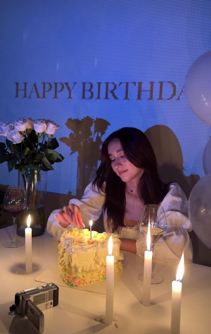 a woman sitting in front of a birthday cake with lit candles