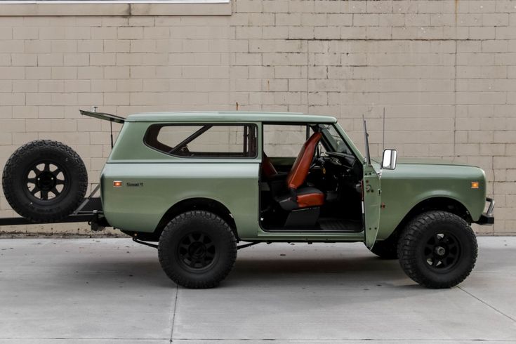 an old green truck parked in front of a brick building with its door open and the driver's seat up