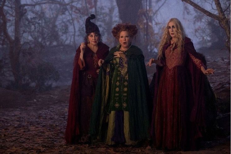 three women dressed in medieval costumes standing next to each other on a forest floor at night