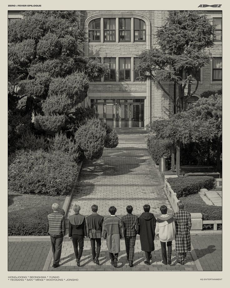 four people standing in front of a large building with trees on each side and bushes to the other side