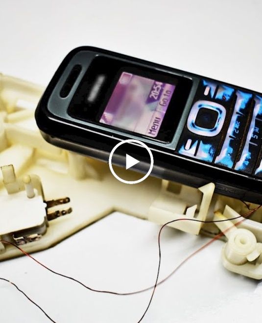 a cell phone sitting on top of a piece of white plastic with wires attached to it