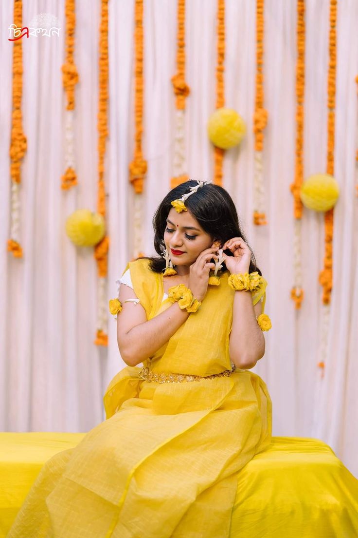 a woman in a yellow dress is talking on her cell phone while sitting down with flowers hanging from the wall behind her