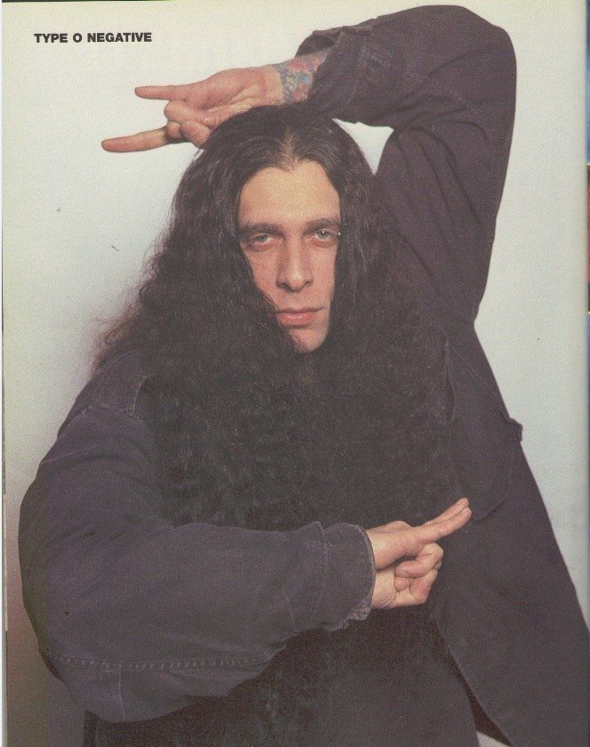 a man with long black hair holding his hands on his head and pointing to the side