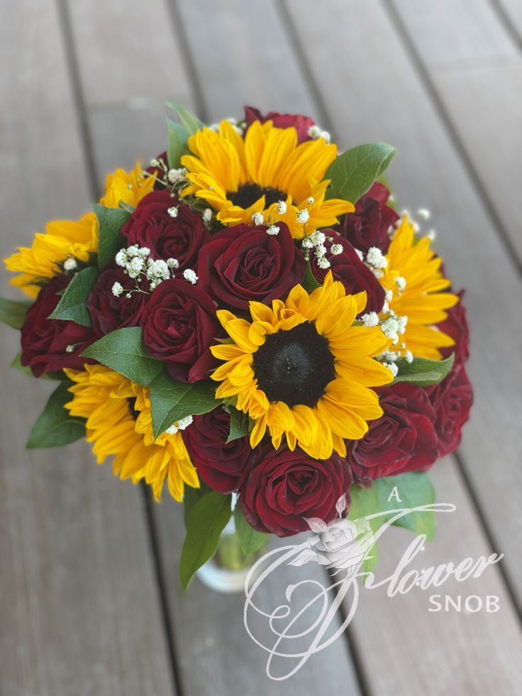 a bouquet of sunflowers and roses in a glass vase on a wooden floor