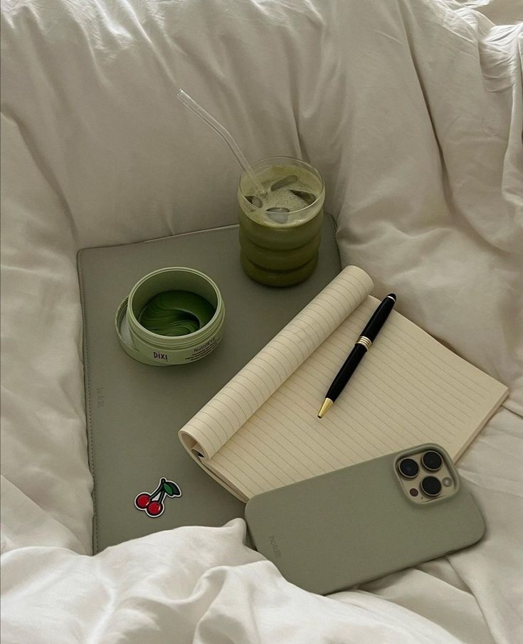 a notepad, pen and cup sitting on top of a bed