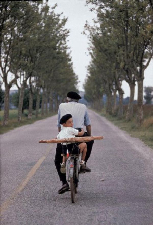 a man riding on the back of a bike down a road next to a little boy