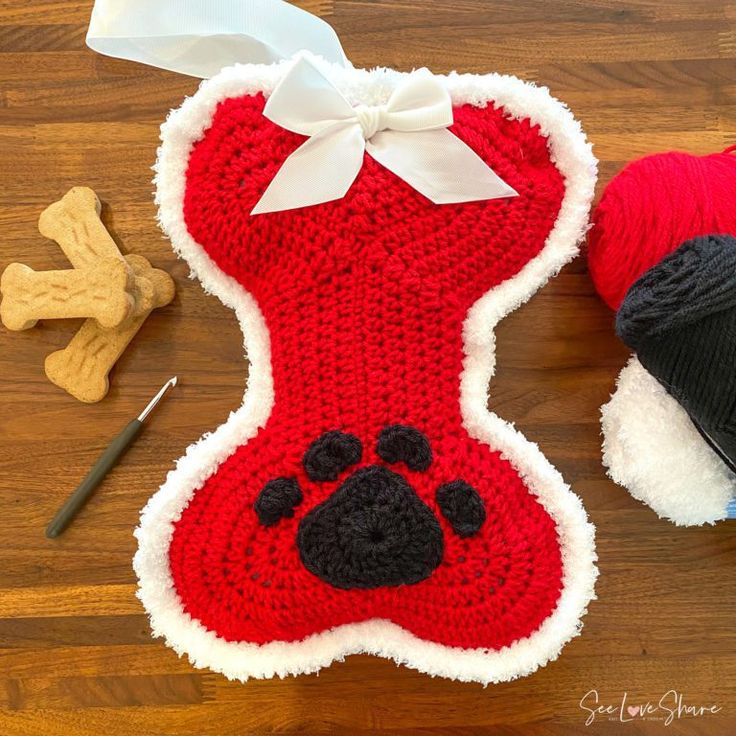 a crocheted dog bone with a red sweater and white bow on it next to a ball of yarn