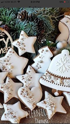 christmas cookies decorated with white icing and decorations on a table next to pine cones