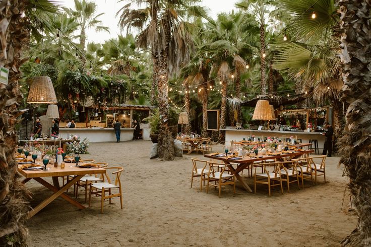 tables and chairs are set up in the middle of a sandy area with palm trees