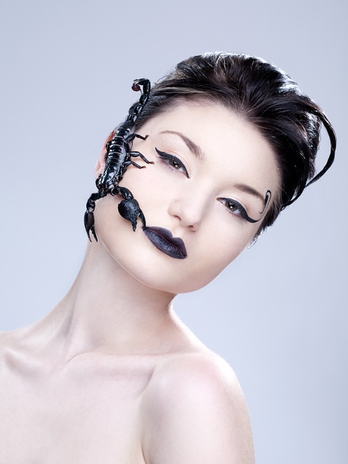 a woman with scorpion tattoos on her face and chest, looking at the camera while wearing black lipstick