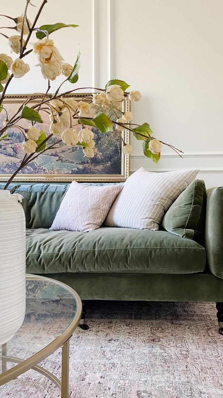 a living room with a green couch and flowers in the vase on the coffee table