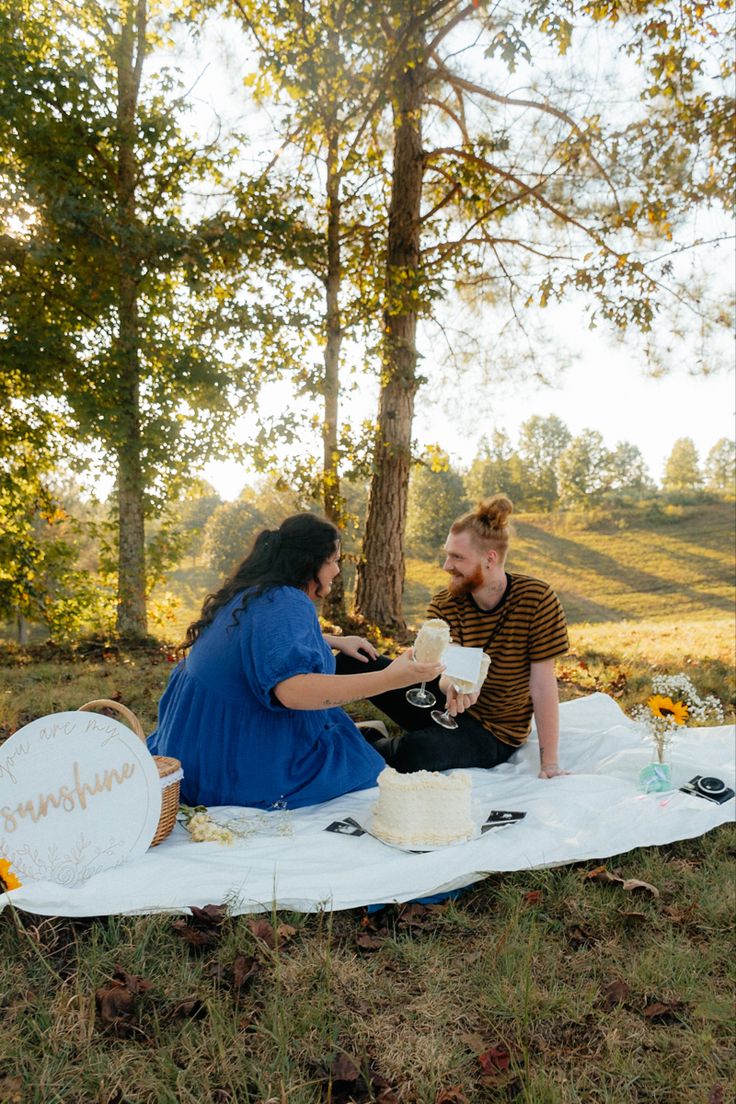 a man and woman are sitting on a blanket in the woods, having a picnic