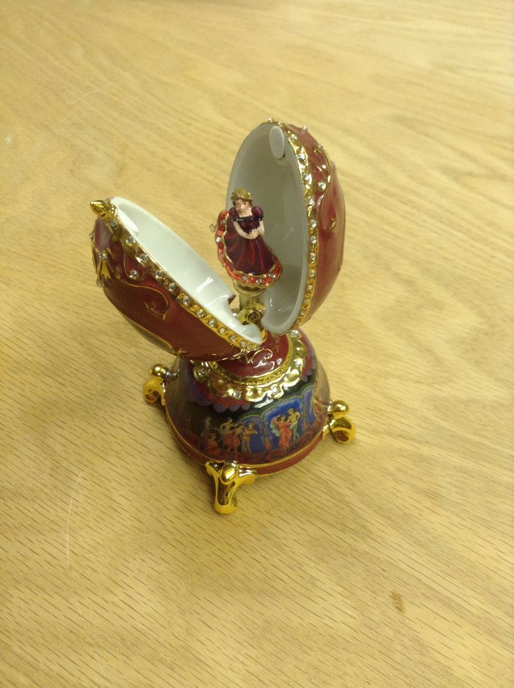 an ornate red and gold vase sitting on top of a wooden table next to a small figurine