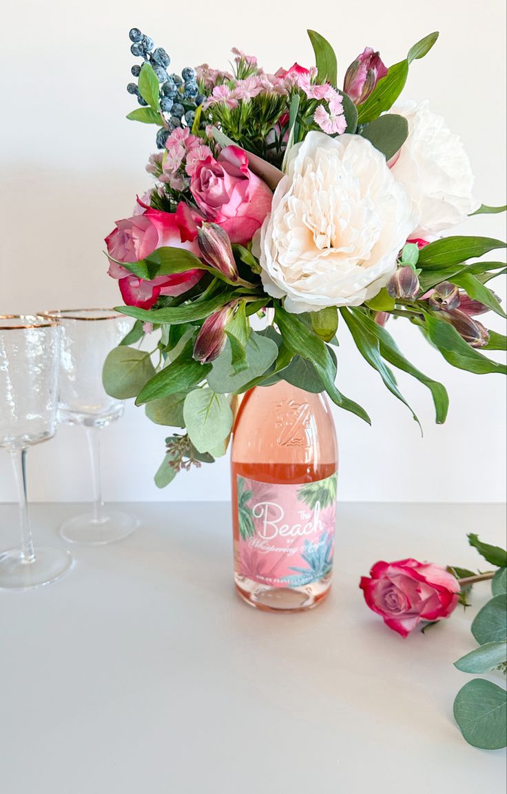 a vase filled with pink and white flowers on top of a table next to two wine glasses