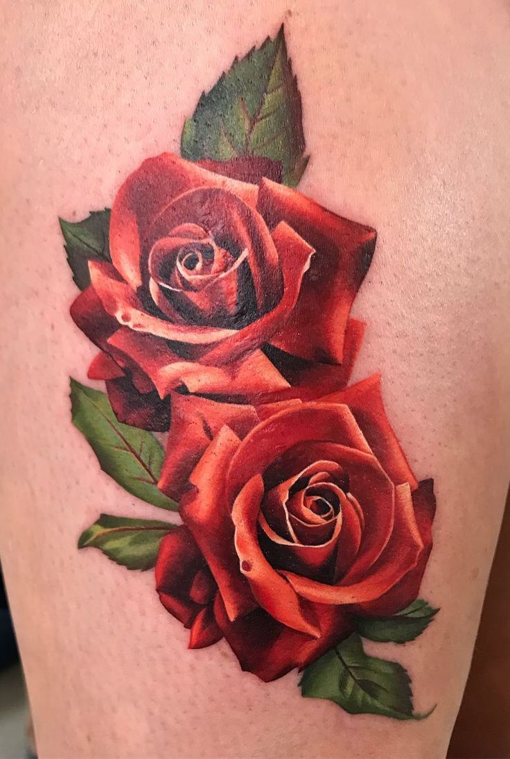 a woman's thigh with two red roses on it and green leaves around the thighs