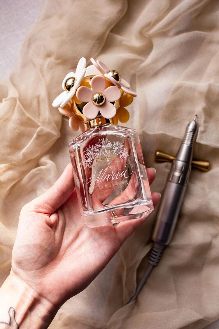 a person holding a small bottle with flowers on it and a pen next to it