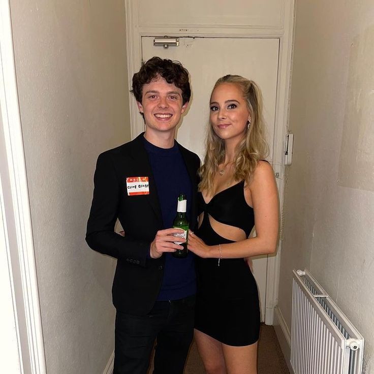 a young man and woman standing next to each other in a hallway holding beer bottles