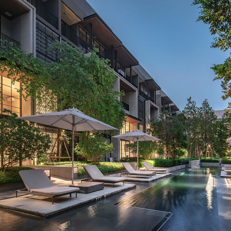 an outdoor swimming pool with lounge chairs and umbrellas next to the building at dusk