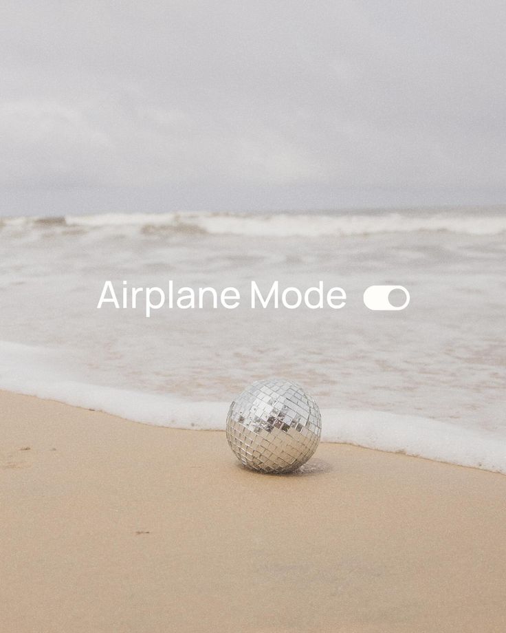 a disco ball sitting on top of a sandy beach next to the ocean with an airplane mode logo above it