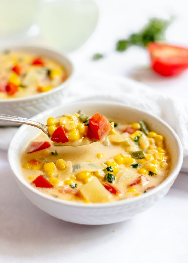 two bowls filled with corn and vegetables on top of a white cloth covered tablecloth