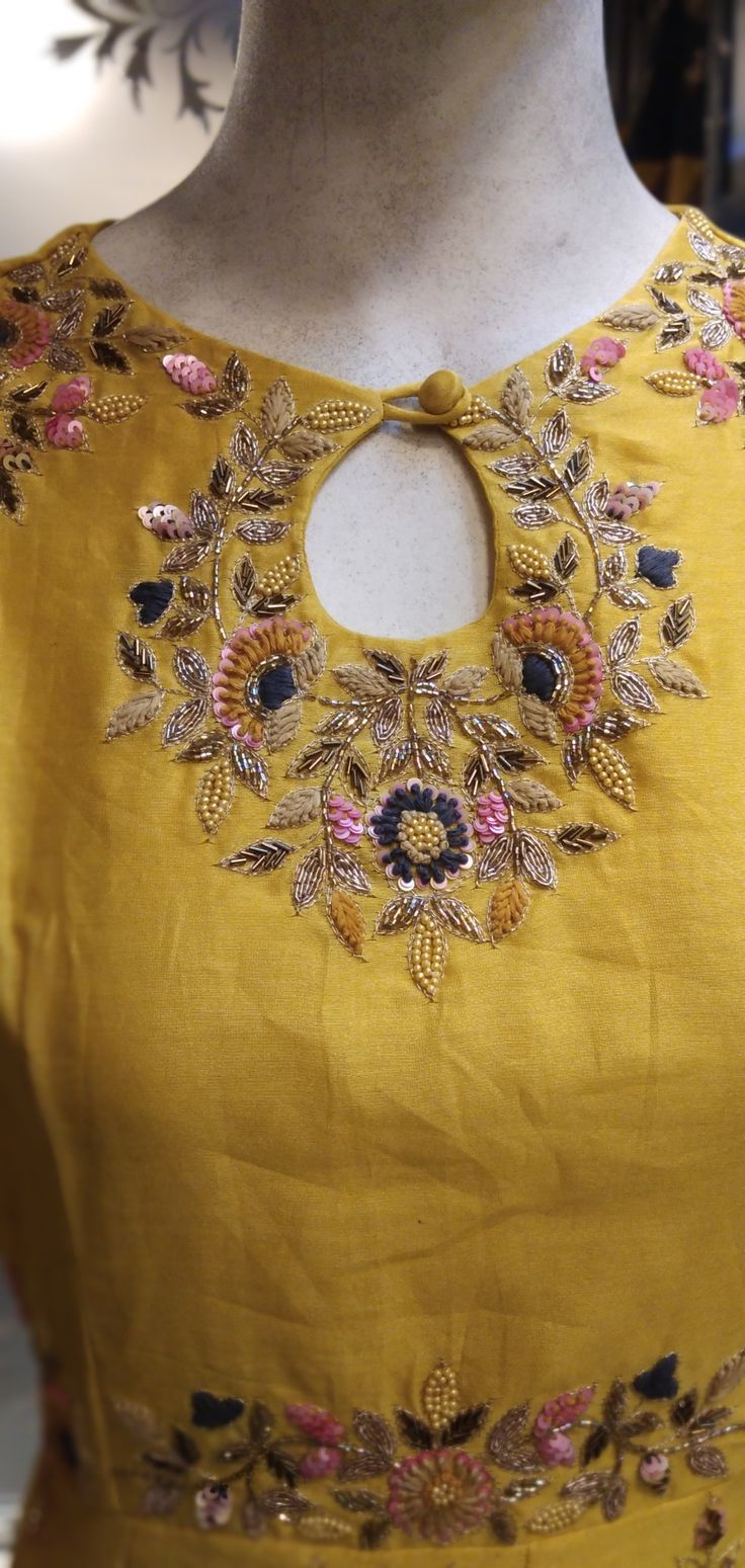 a woman's yellow dress with gold and pink flowers on the neck, in front of a mannequin