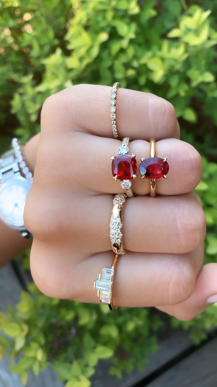 a woman's hand holding three rings with red and white stones on each ring