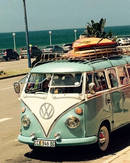 an old vw bus with surfboards on top is driving down the road by the ocean