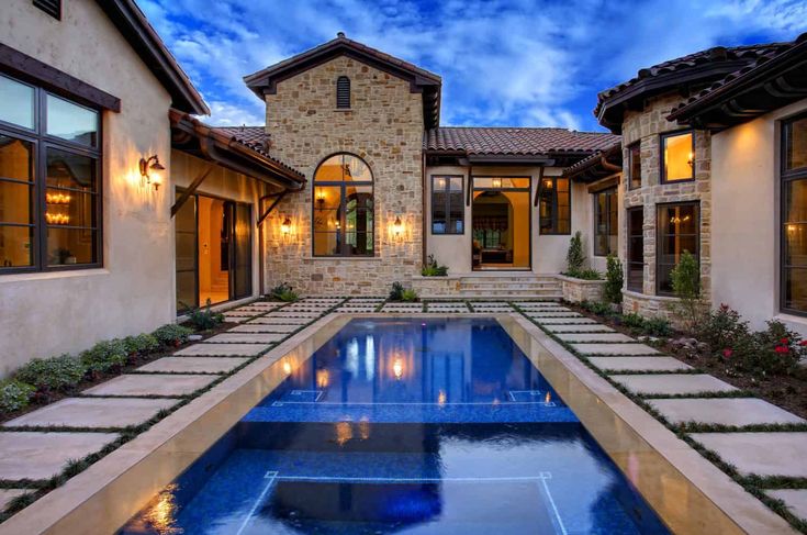 a pool in front of a house with lights on the side and windows above it