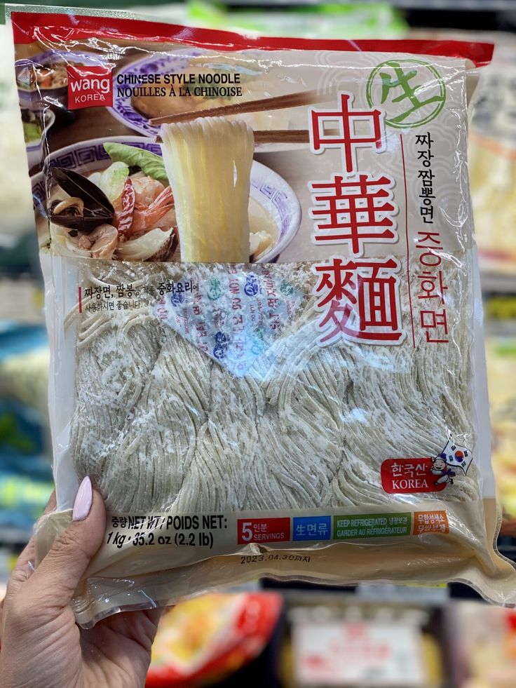 a person holding up a bag of noodles in front of some other food on display