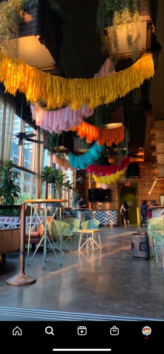 the interior of a restaurant decorated with colorful streamers and potted plants hanging from the ceiling