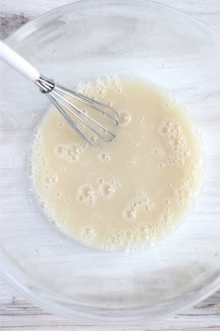 a glass bowl filled with milk and whisk