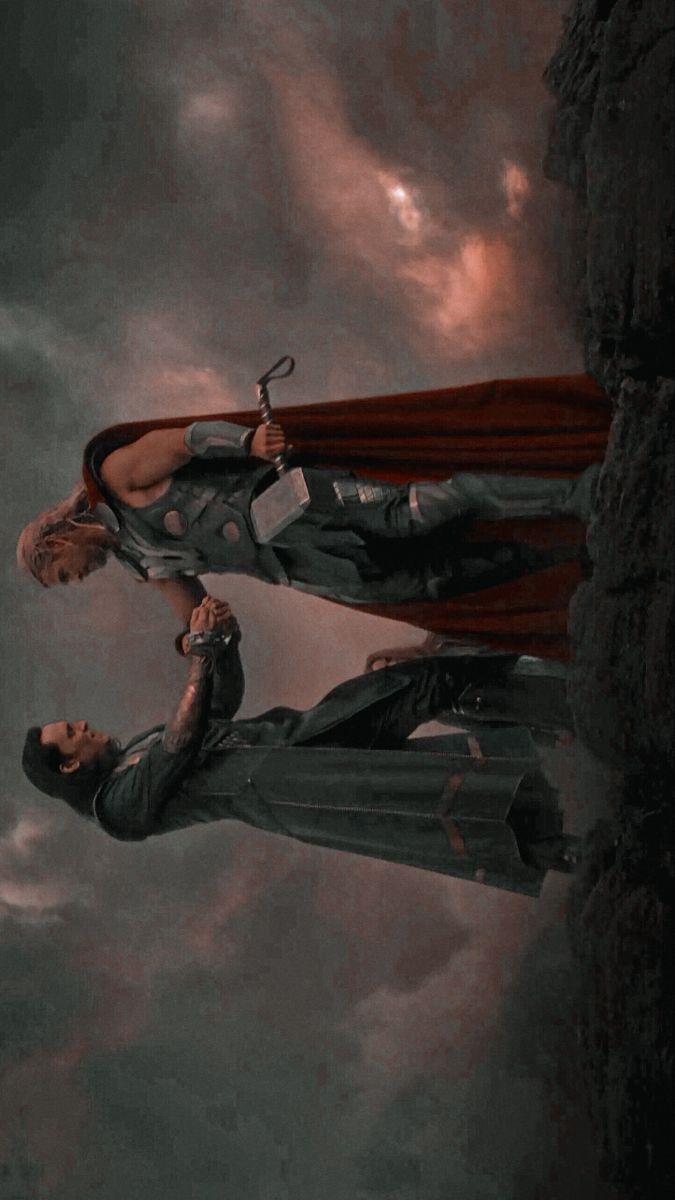 two superheros standing on top of a cliff with one holding the other's hand