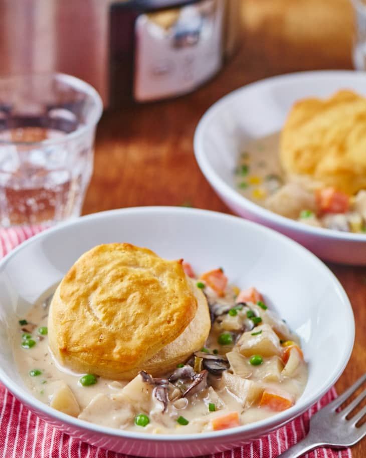 two white bowls filled with food on top of a wooden table next to silverware