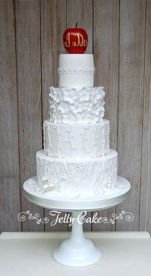 a three tiered wedding cake with an apple on the top and initials on the side