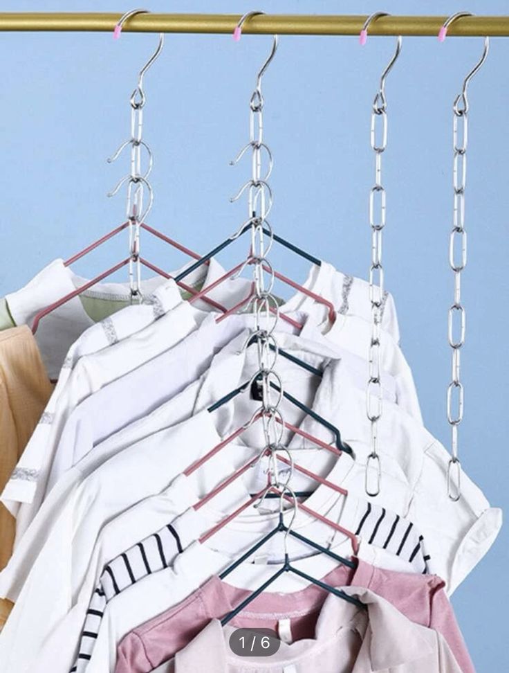 several shirts hanging from a clothes rack with metal chains attached to the hangers, against a blue background