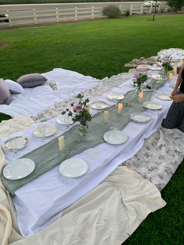 a long table with plates and candles on it in the middle of a grassy field