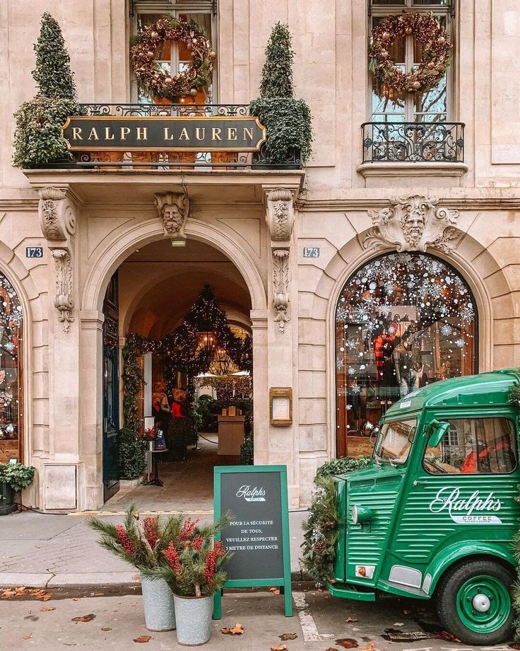 an old green truck parked in front of a building with wreaths on the windows