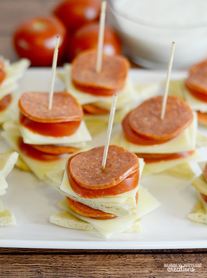 small sandwiches with toothpicks are arranged on a white platter next to tomatoes