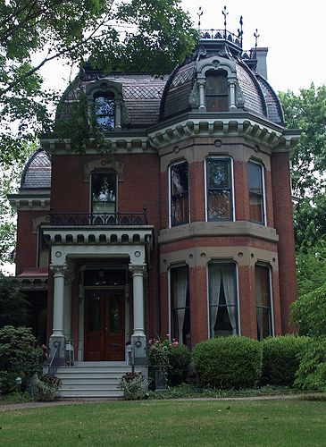 a large red brick house sitting in the middle of a lush green park next to trees