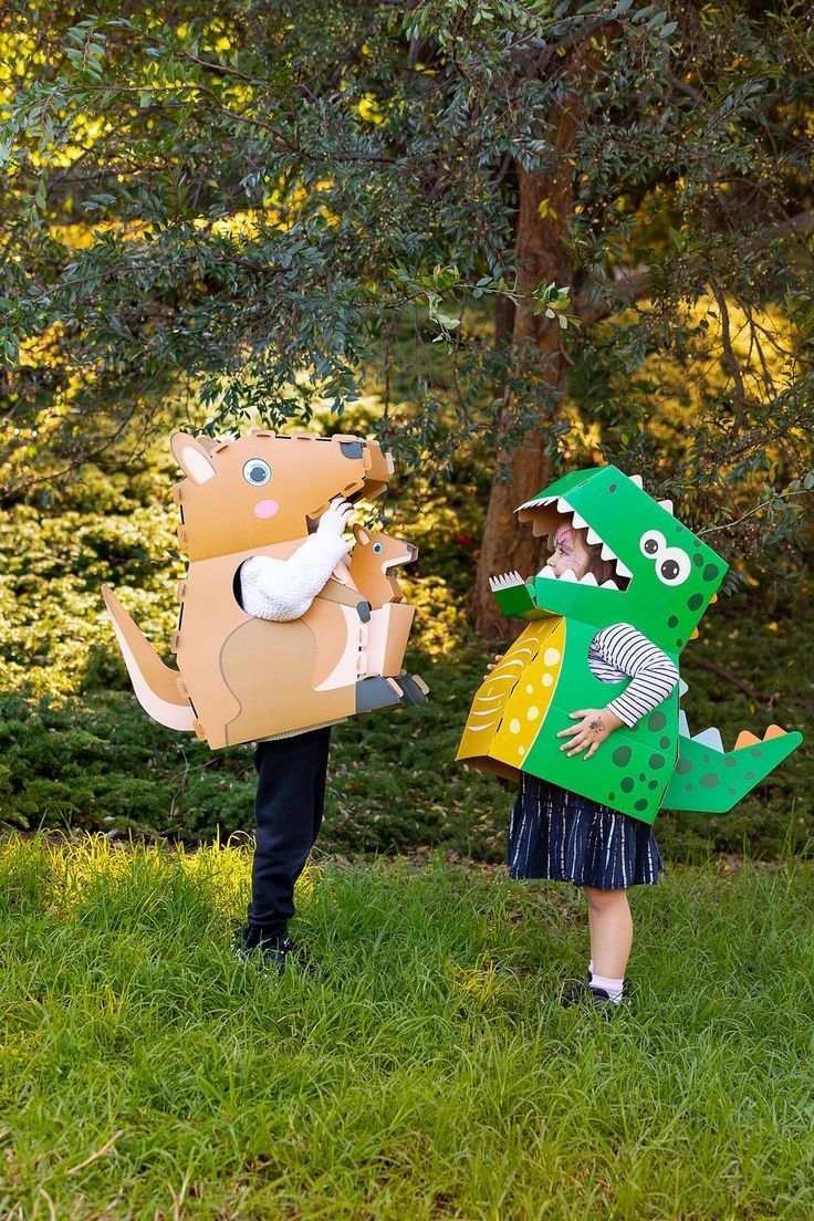 two children dressed up as dinosaurs and alligators, one holding a paper bag in the other's mouth