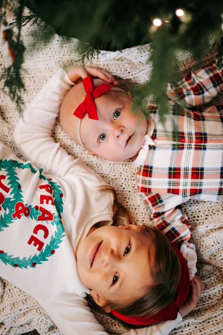 two young children laying next to each other under a christmas tree