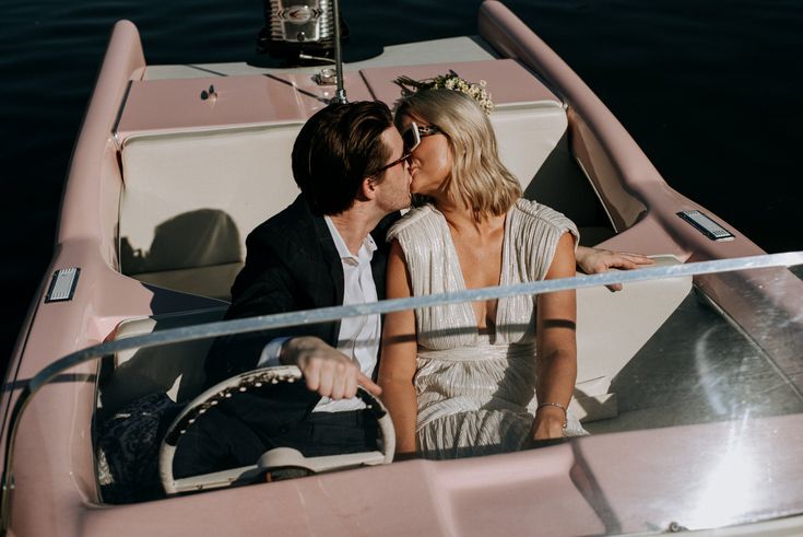 a man and woman sitting in a pink boat on the water with their arms around each other