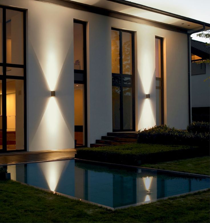 a modern house lit up at night with the lights on and reflecting in the pool