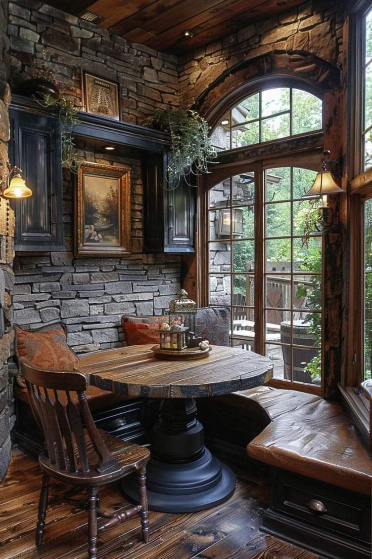 a table and two chairs in a room with stone walls, wood flooring and large windows