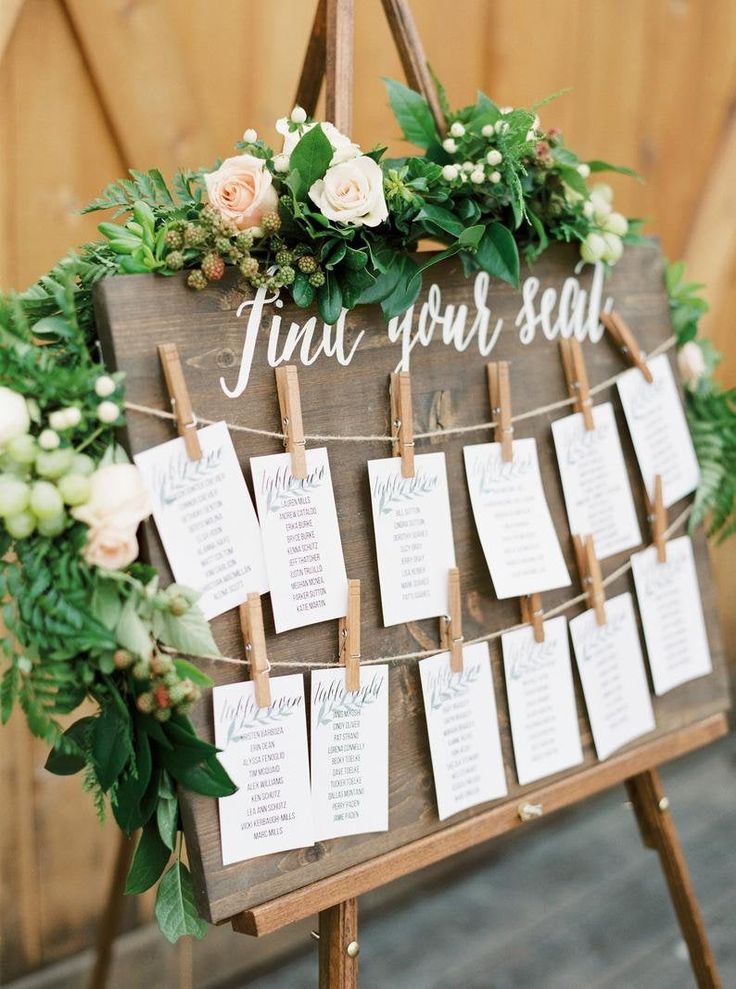 a wooden sign with seating cards attached to it and greenery around the signs that read, find your seat