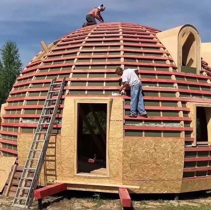 two men working on the roof of a large dome shaped building that is being built