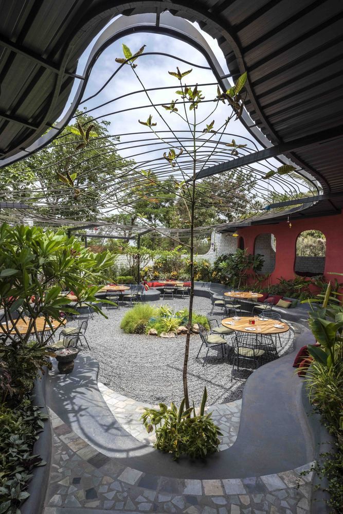 an outdoor seating area with tables and chairs in the center, surrounded by greenery