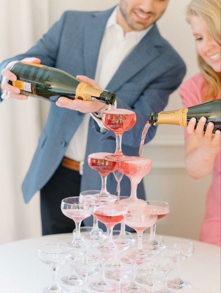 two people pouring champagne into wine glasses on top of a table with another person in the background