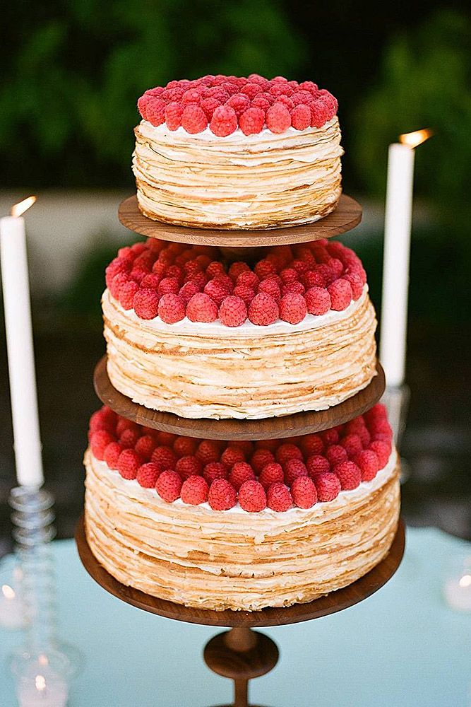 a three tiered cake with raspberries on top and candles in the background